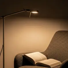 Przytulny fotel z otwartą książką, oświetlony przez lampę podłogową do czytania regulowaną. Idealne miejsce na relaks.