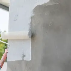 Malowanie betonu architektonicznego wałkiem na biało. Widać proces odświeżania powierzchni.
