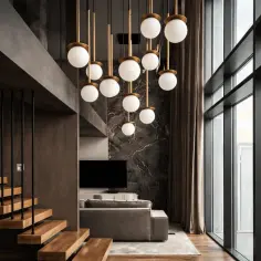 Nowoczesna lampa z kulistymi kloszami ze szkła dymionego, wisząca nad salonem z marmurową ścianą i drewnianymi schodami.