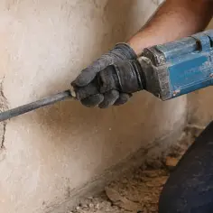 Rękawice i młot udarowy pomagają w tym, jak usunąć tynk dekoracyjny ze ściany.