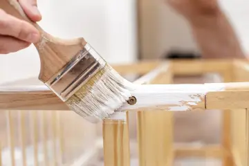 Malowanie białym lakierem mebli z okleiny. Pędzel nakłada farbę na drewnianą ramę, odnawiając jej wygląd.